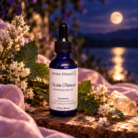 Aries Moon White Patchouli Hair Oil in a blue dropper bottle surrounded by white flowers beside moonlit water.